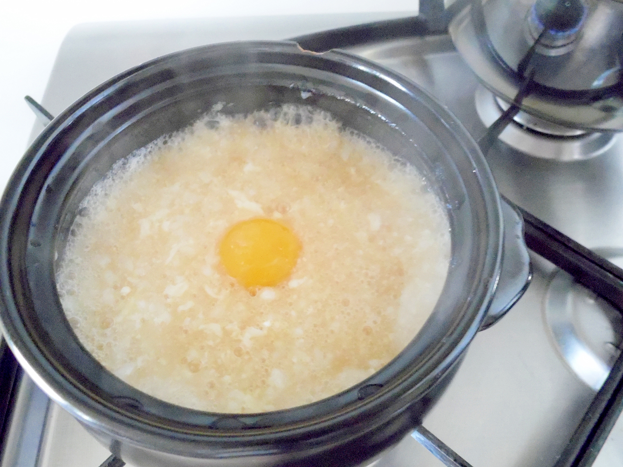 黒い鍋に入った生卵のせおかゆ