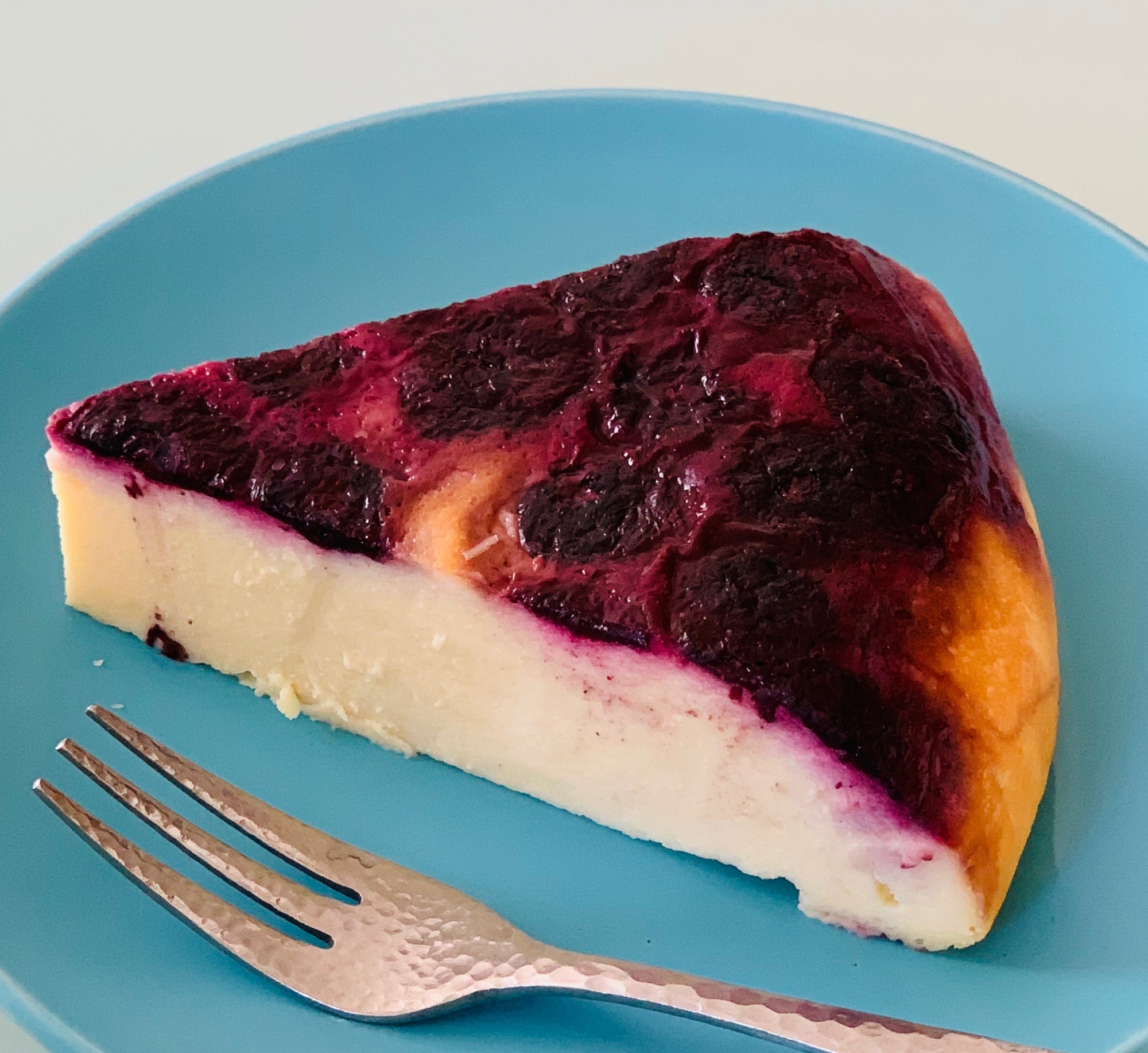 青い丸皿にのった、表面にブルーベリーが入っているチーズケーキ