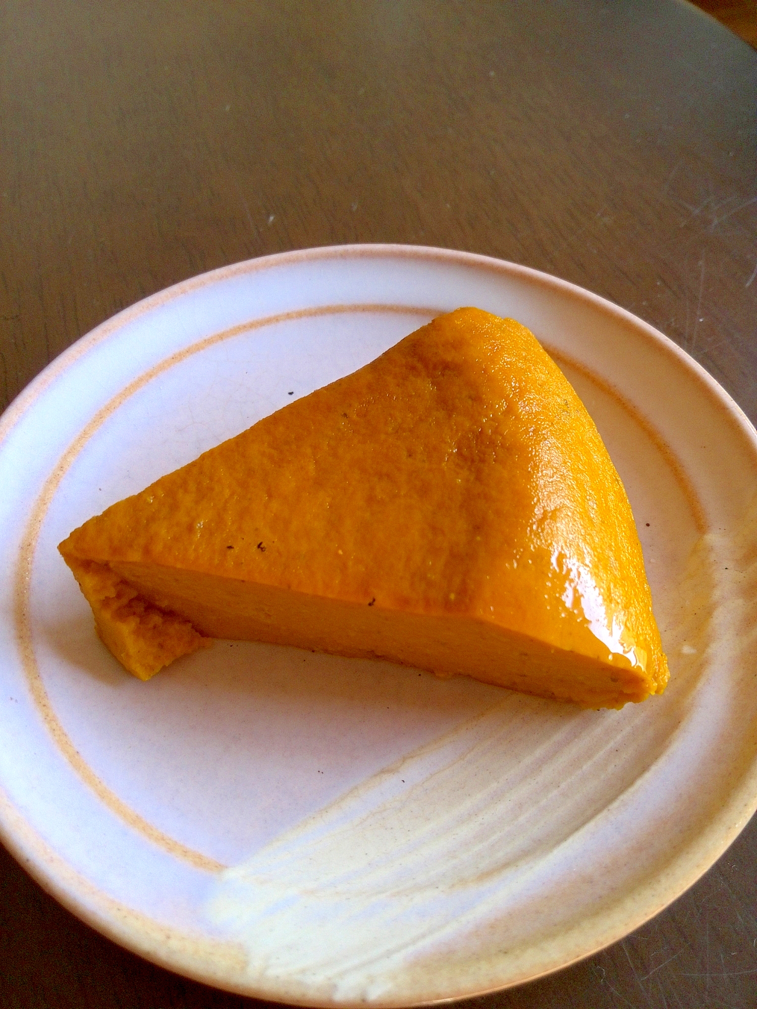 縁取りに黄色いラインの入った白い器にかぼちゃのプリンが一切れ盛られている。