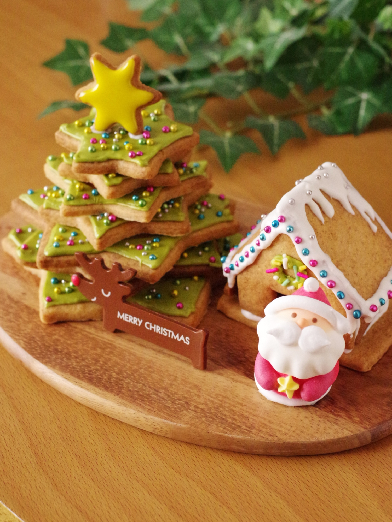 アイシングクッキーが積み重なったツリーと立体的なクッキーの家がのっている木製皿