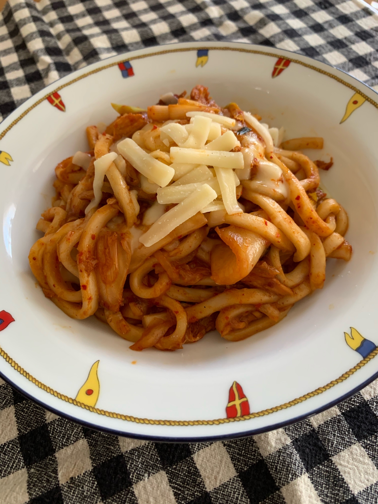 模様入りの皿に盛りつけられた、ツナとチーズのキムチ焼きうどん