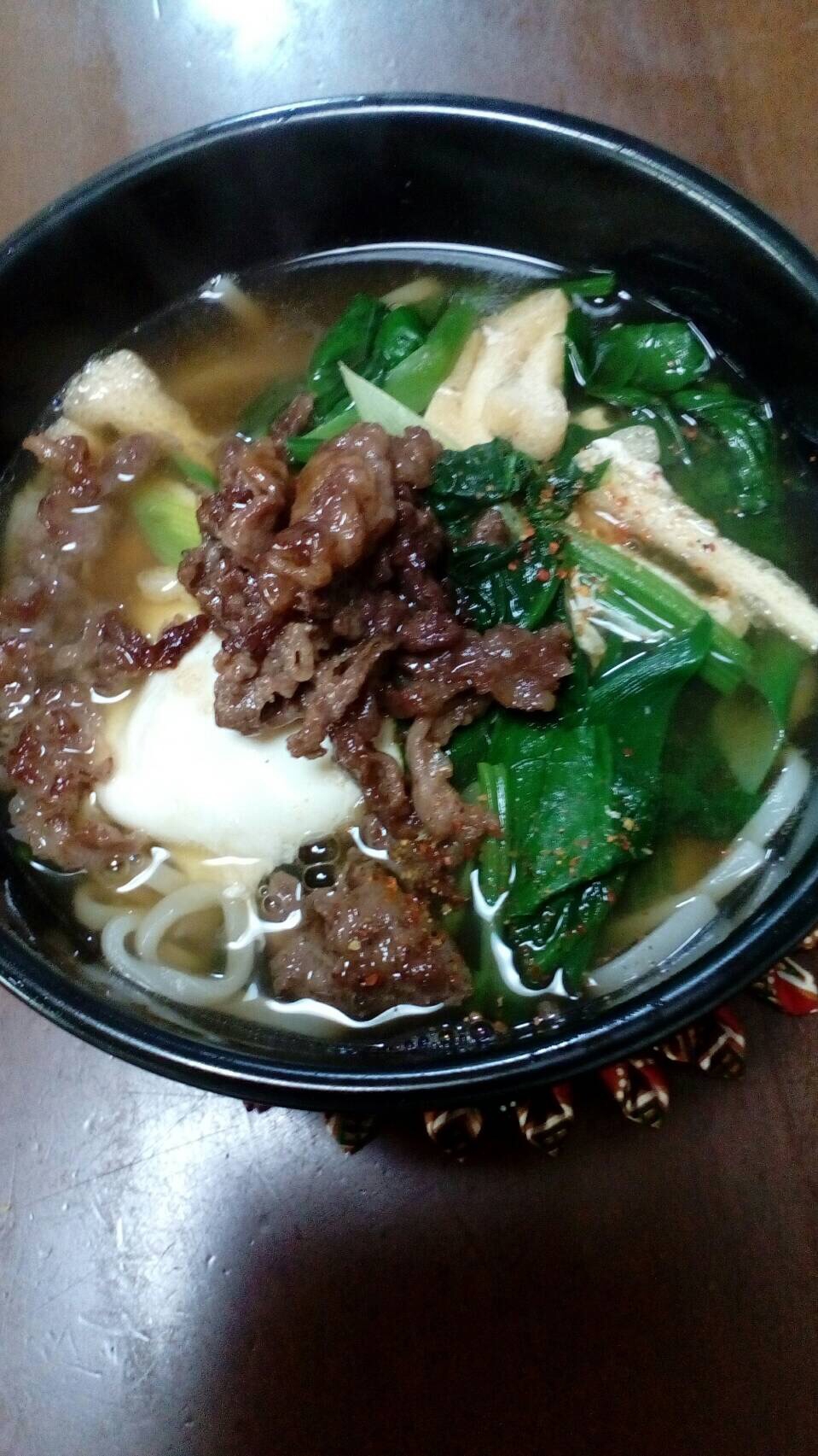 黒い器に盛り付けられている牛肉とほうれん草の温うどん