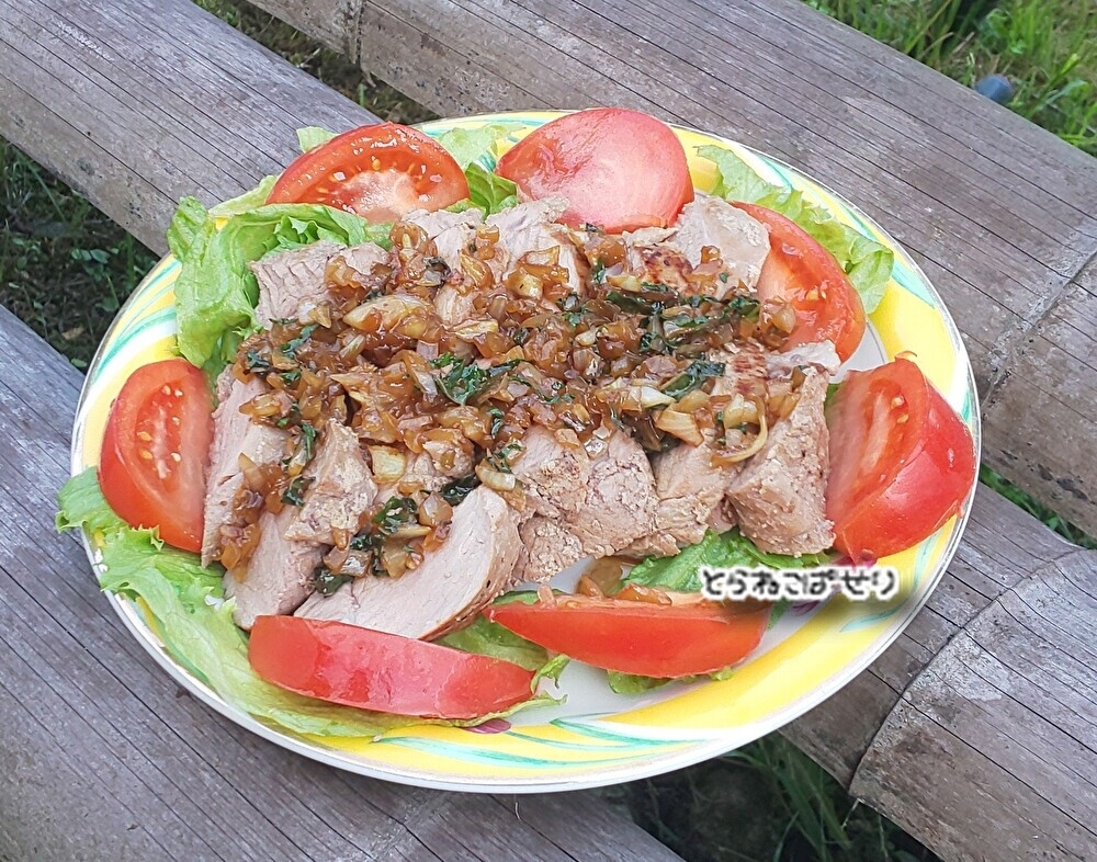 黄色いふちの丸皿にトマトや生野菜とともに盛り付けられたローストポーク