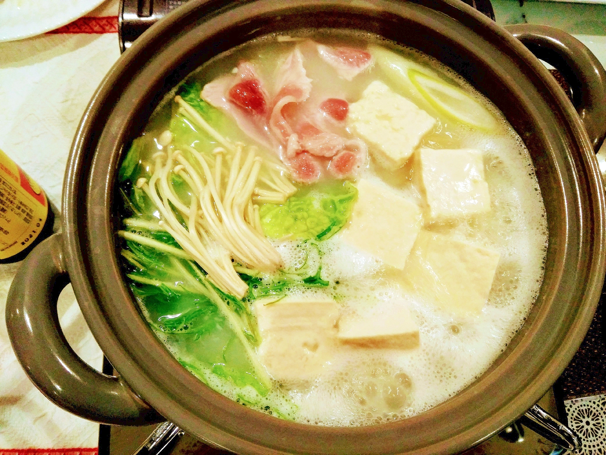 茶色の土鍋に入っている、豚しゃぶと野菜たっぷりな湯豆腐