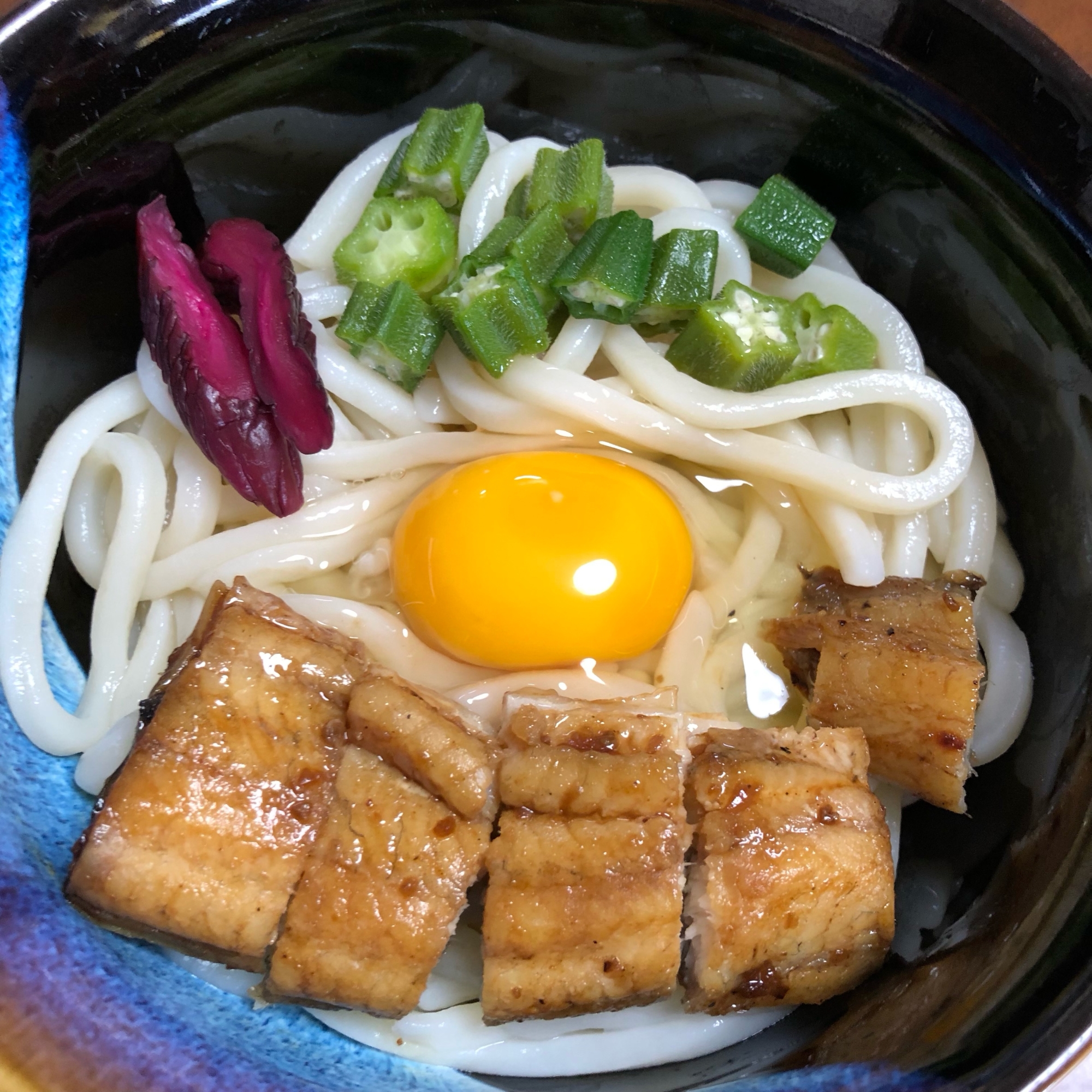 黒い器に盛りつけたうなぎとオクラの釜玉うどん