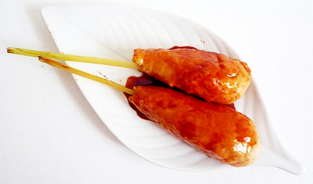 葉形の白い皿に盛りつけられている2本の鶏つくね照り焼き