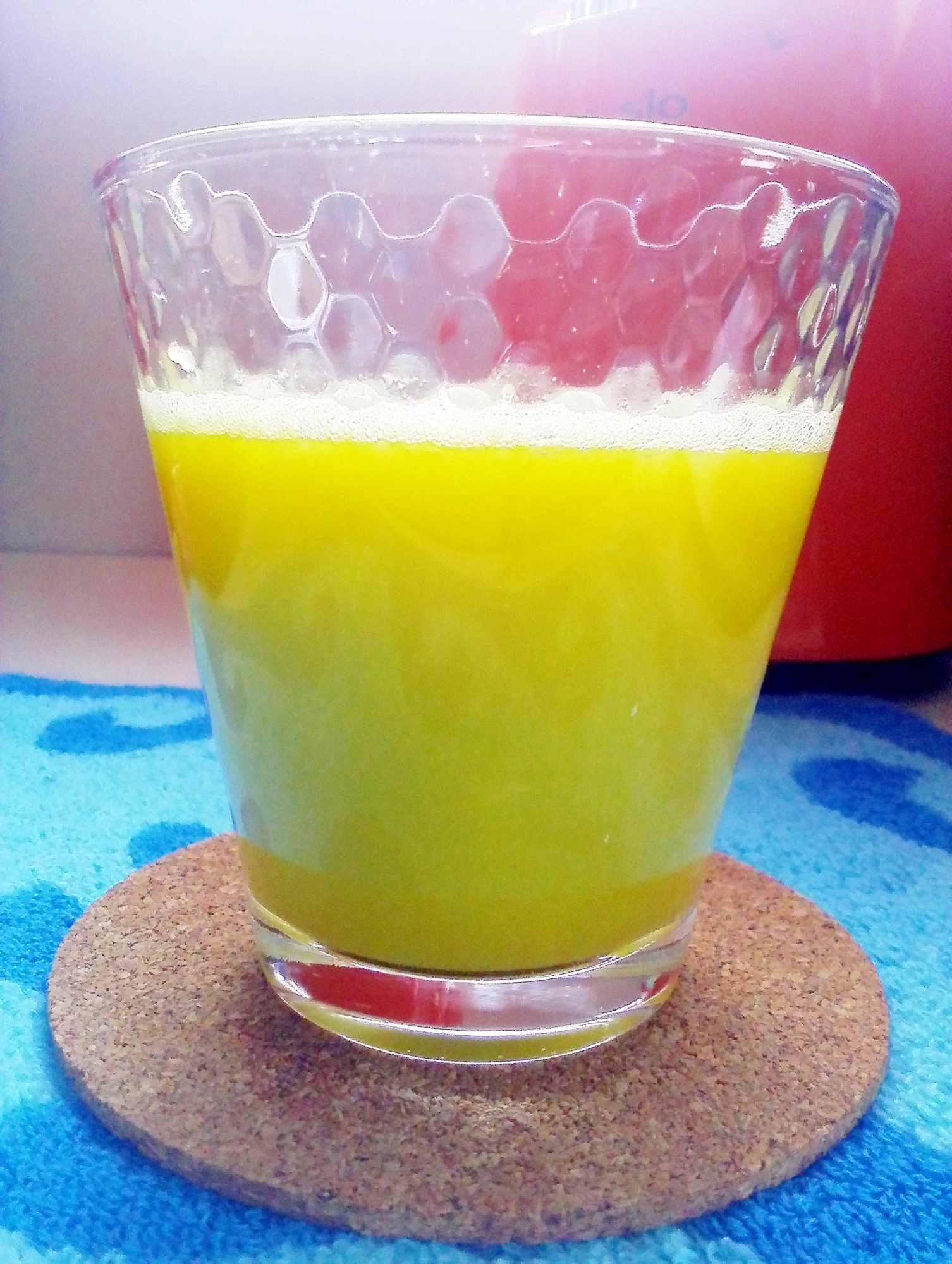 コルクのコースターにのせられた透明グラスに入っている、キウイとオレンジのコールドプレスジュース