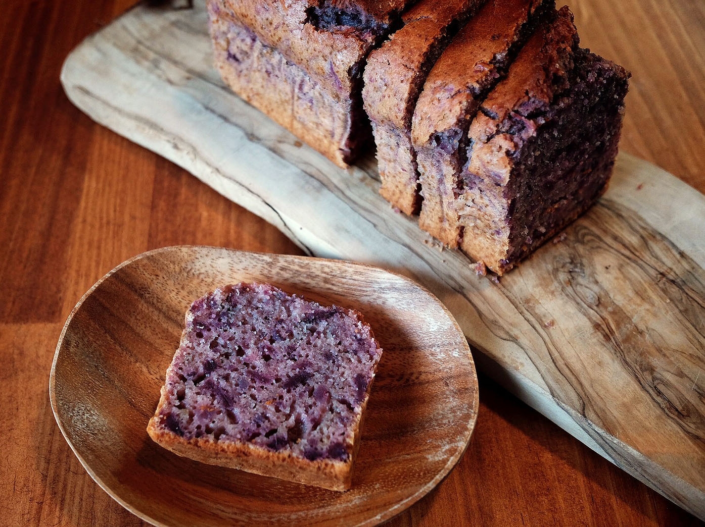 木目がしっかり出た細長いカッティングボードと木皿に盛られた紫芋のパウンドケーキ