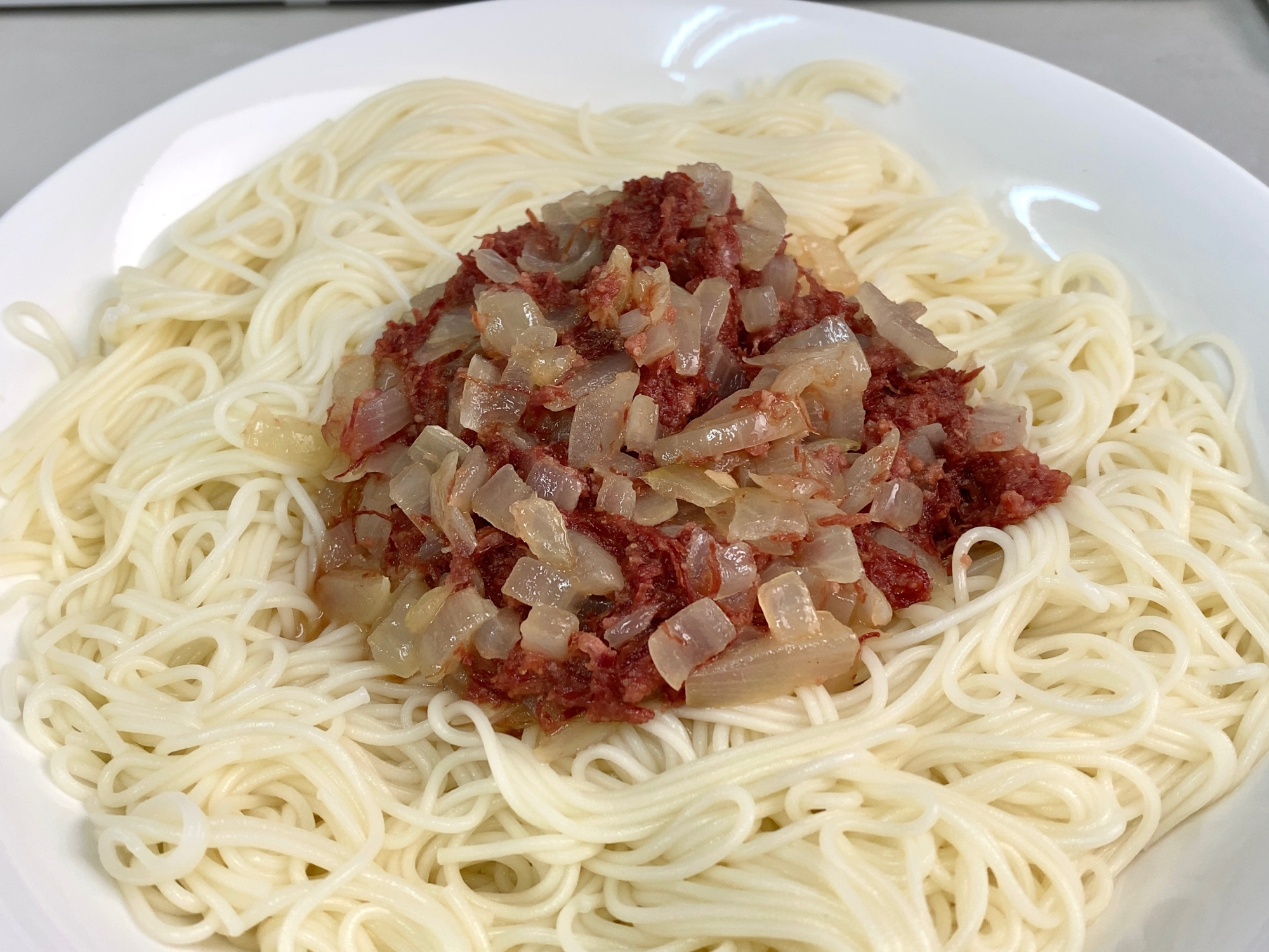 コンビーフと玉ねぎがトッピングされたバター炒めそうめんが白い皿に盛り付けられているところ