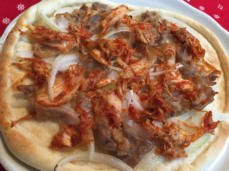 白いお皿に盛られた豚肉とキムチのオニオンピザ