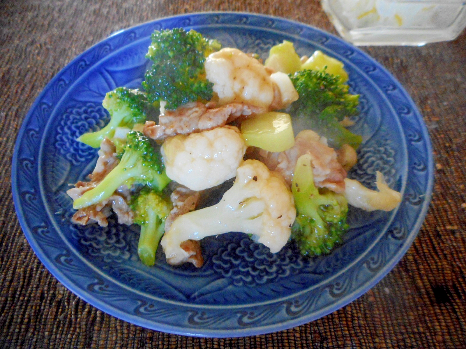 青い丸皿に盛り付けた豚肉とブロッコリーとカリフラワーの中華炒め