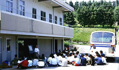 農機具庫の前で作業の説明を聴く学生