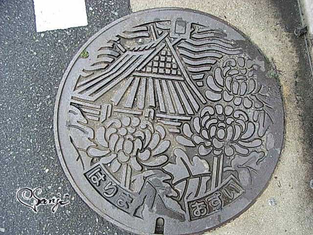 播磨町の花「菊」と大中遺跡の復元住居がデザインされた播磨町のマンホールの蓋。