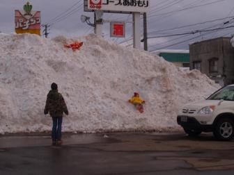 生協の駐車場に出来た雪捨て場の雪山で遊ぶ子供と見守る母親